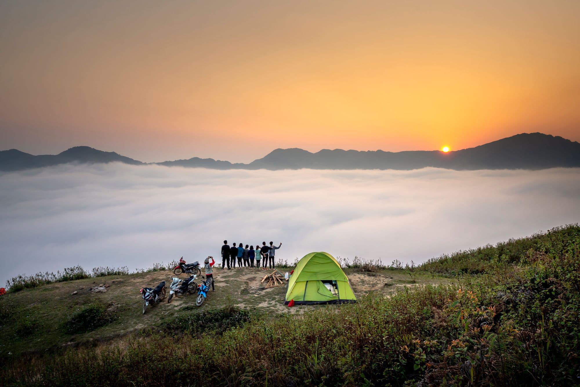 A group of friends watching the sunrise over a sea of clouds from a mountain ridge